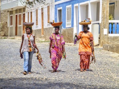 Femmes capverdiennes en robes colorées marchant dans une rue pavée bordée de maisons traditionnelles au Cap-Vert, au cœur de la culture locale