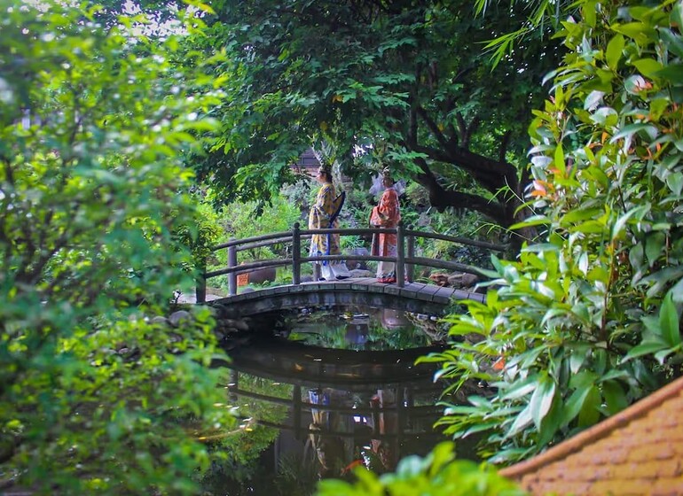 Deux personnes en costumes traditionnels sur un pont de pierre dans le jardin d’Ancient Hué