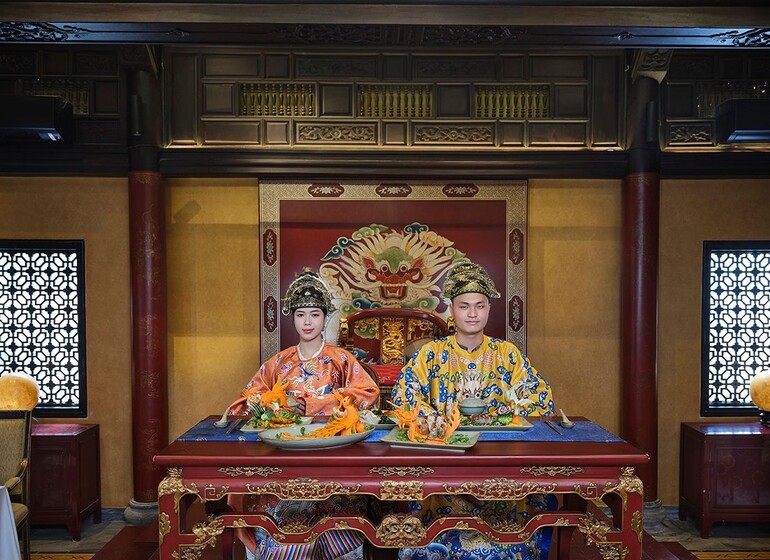 Deux convives en costumes de cour impériale à une table sculptée, dîner royal à Phú Mộng, Ancient Hue